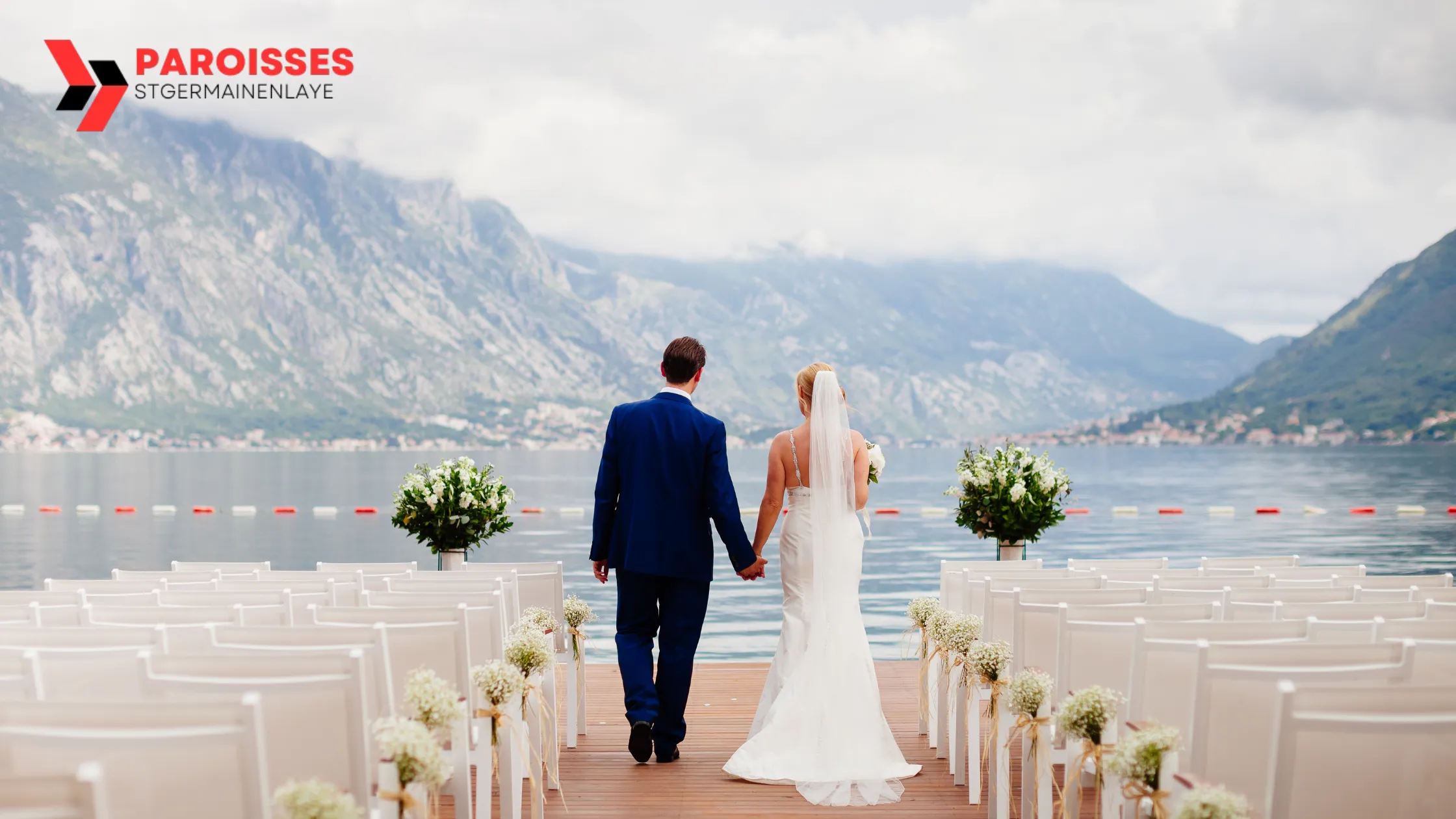 "Can You Get Invited to a Wedding?" A bride and groom walk hand-in-hand down an aisle of white chairs, set against a stunning lakeside backdrop with mountains in the distance, creating a breathtaking and serene wedding atmosphere.